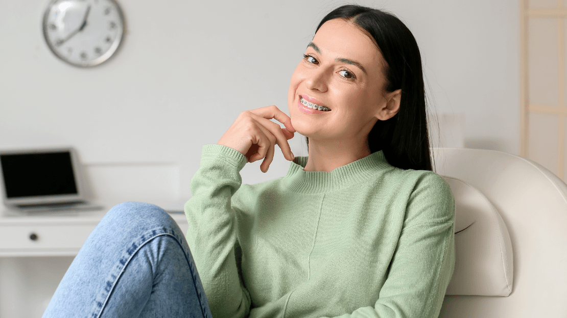 Woman with braces in green sweater smiling on a chair