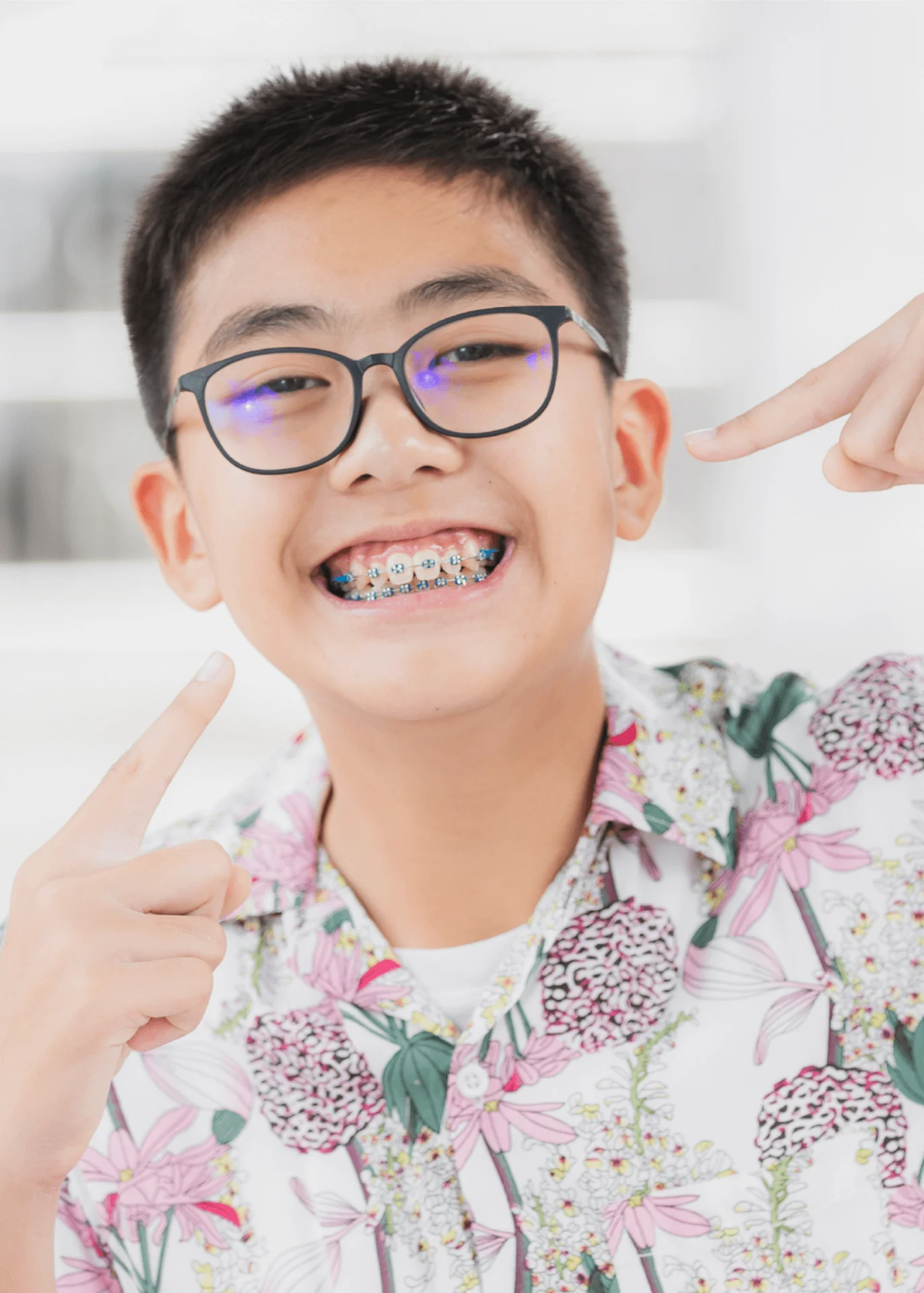 Smiling boy in glasses pointing at his colorful metal braces