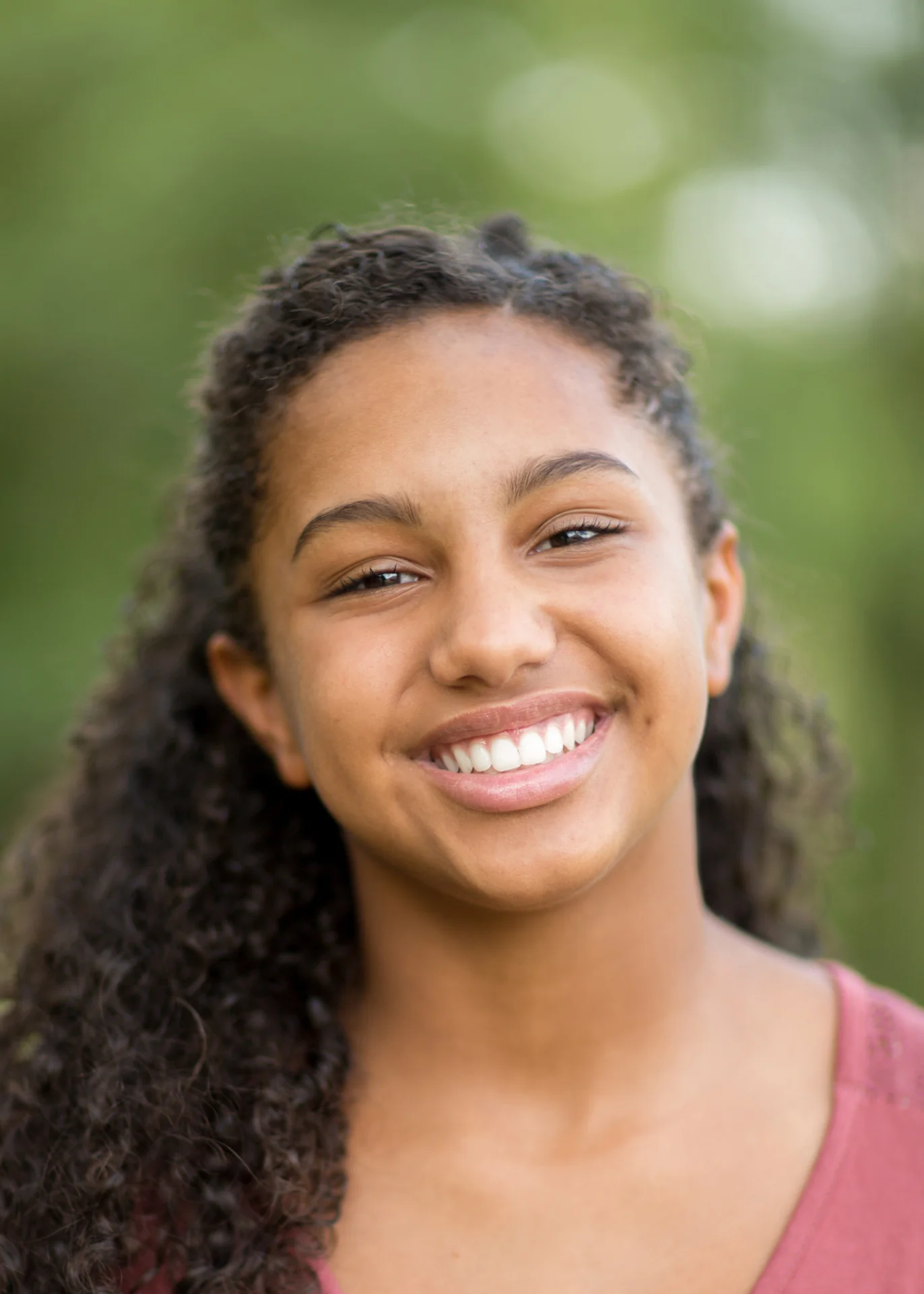 Smiling teen girl with curly hair outdoors with a bright natural smile