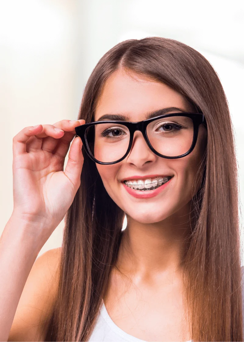 Young woman with long hair smiling to show ceramic braces while adjusting glasses