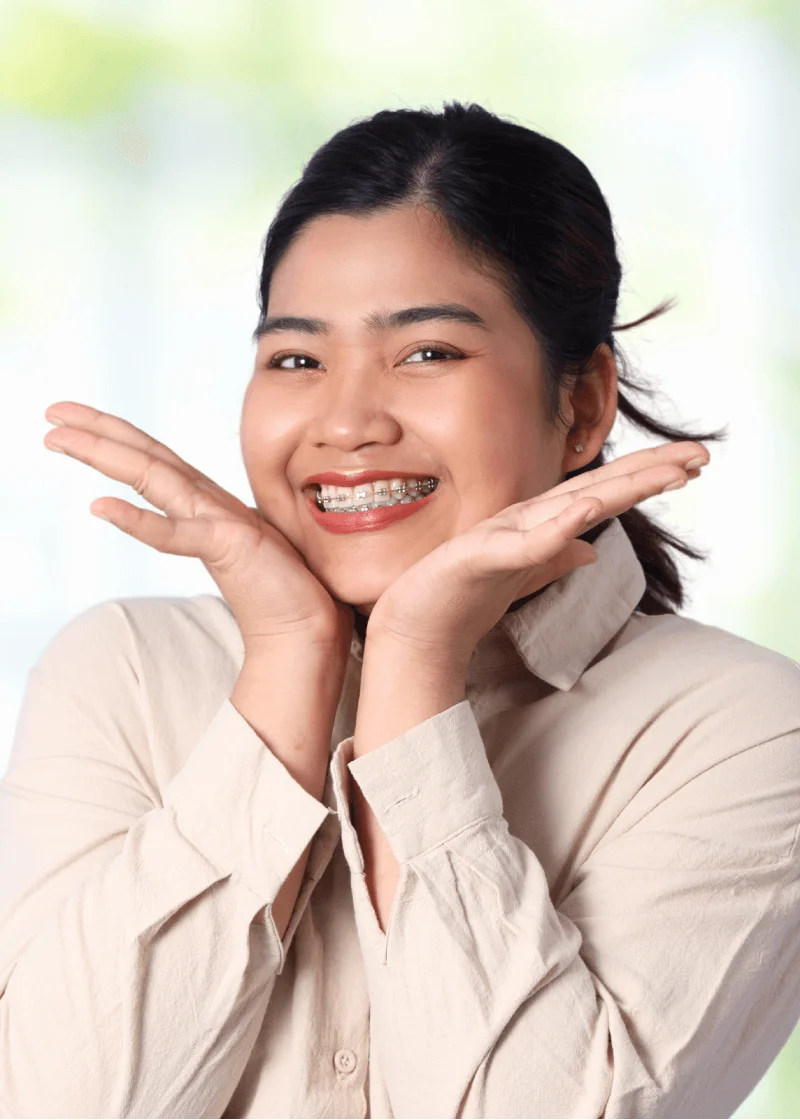 Smiling young woman with metal braces framing her face with her hands