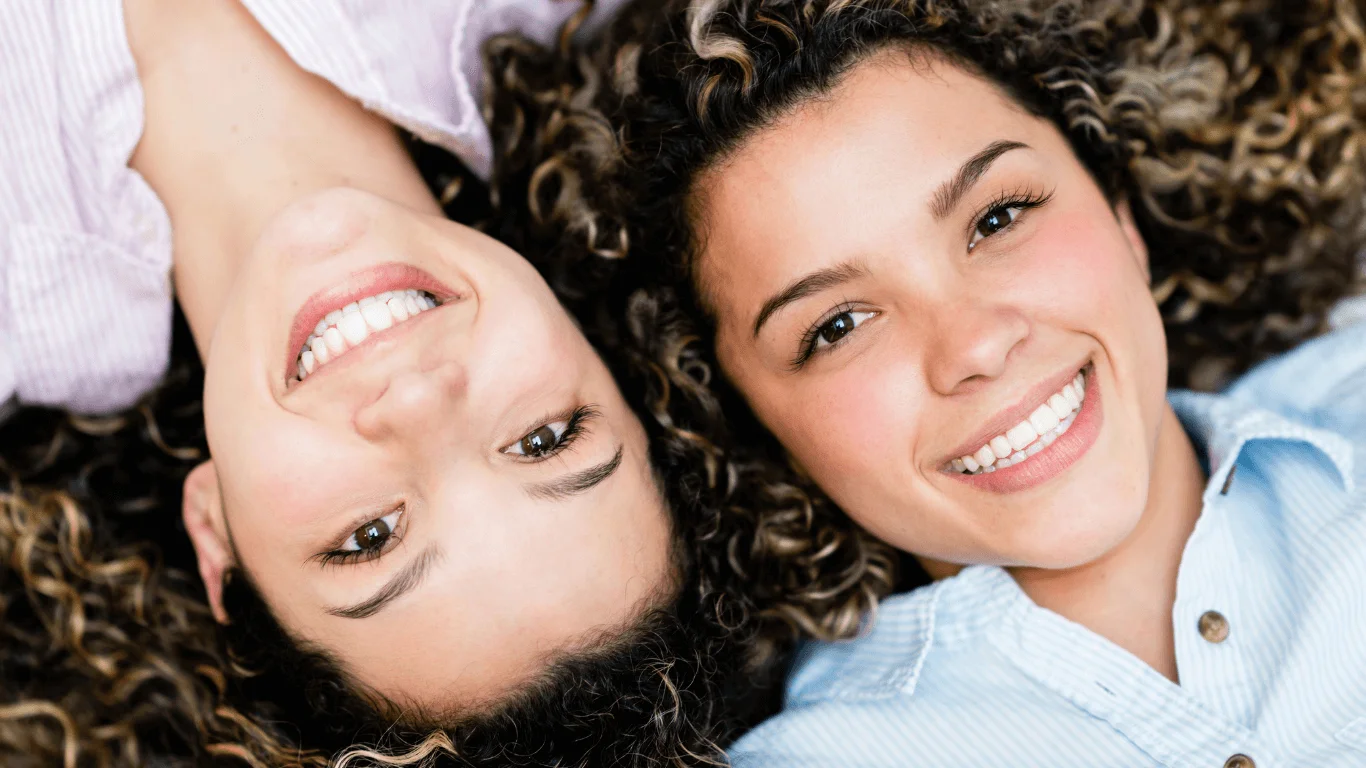 Two friends lying head to head smiling with bright straight teeth
