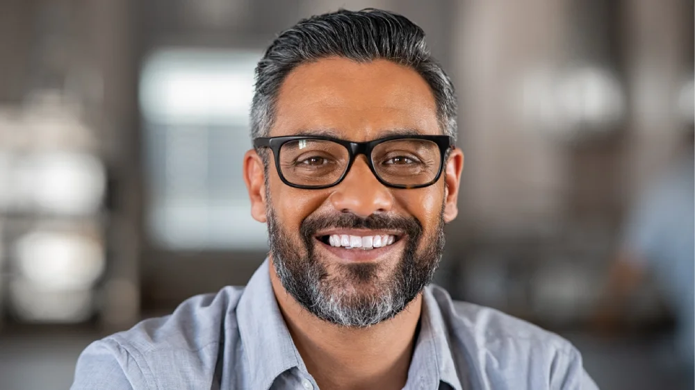 Smiling middle-aged man in glasses and a gray shirt with a confident smile