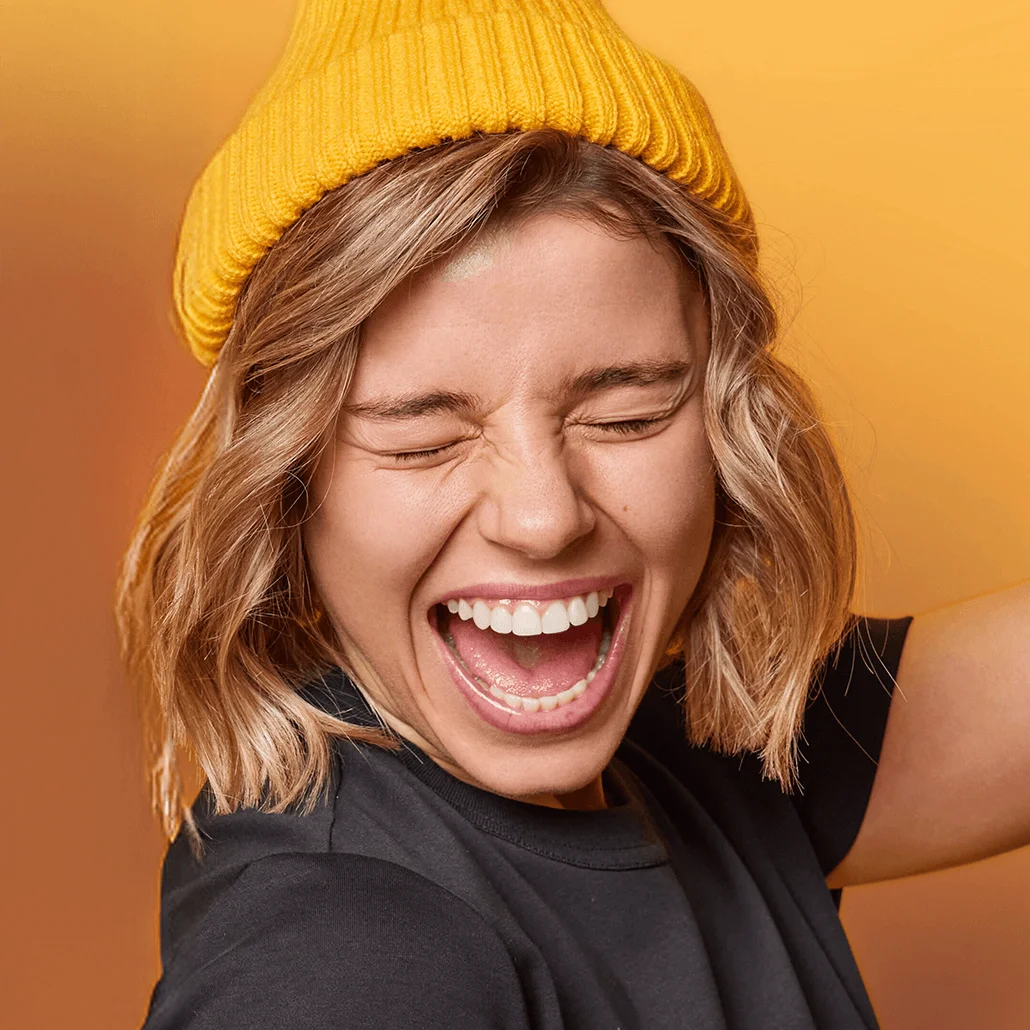 Young woman in a yellow beanie laughing with a wide open smile
