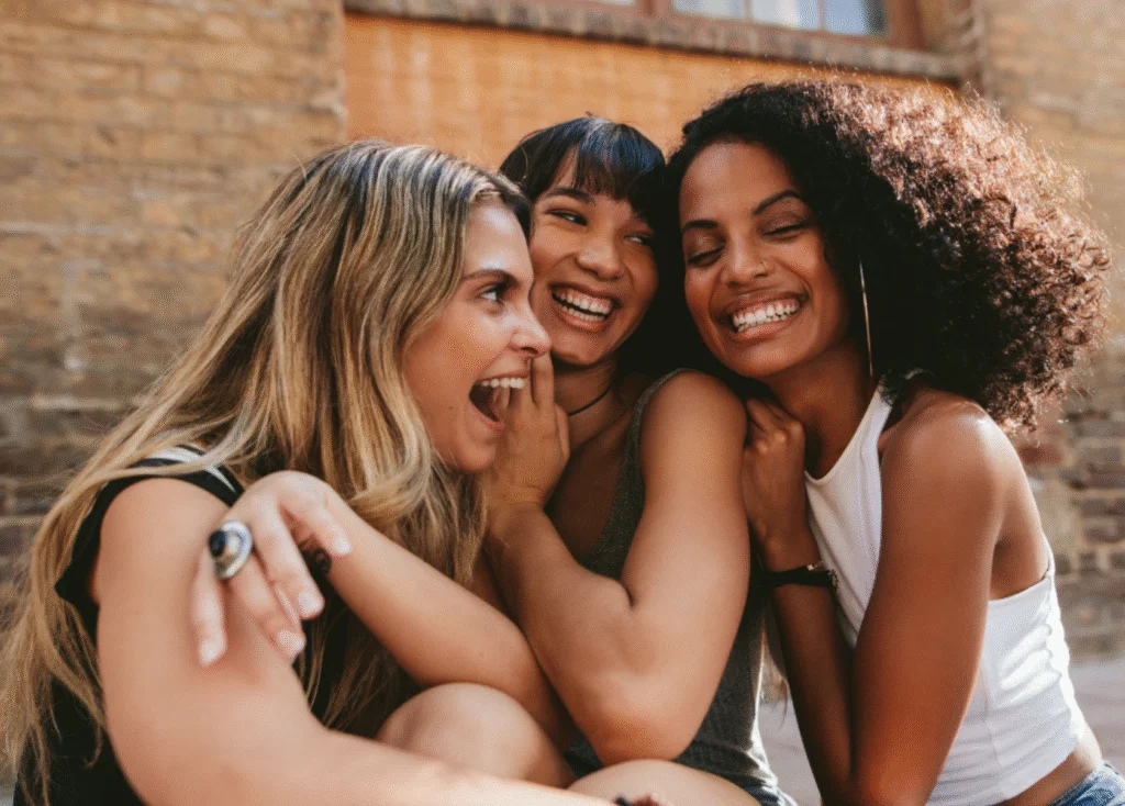 Three young women friends laughing and embracing against a brick wall