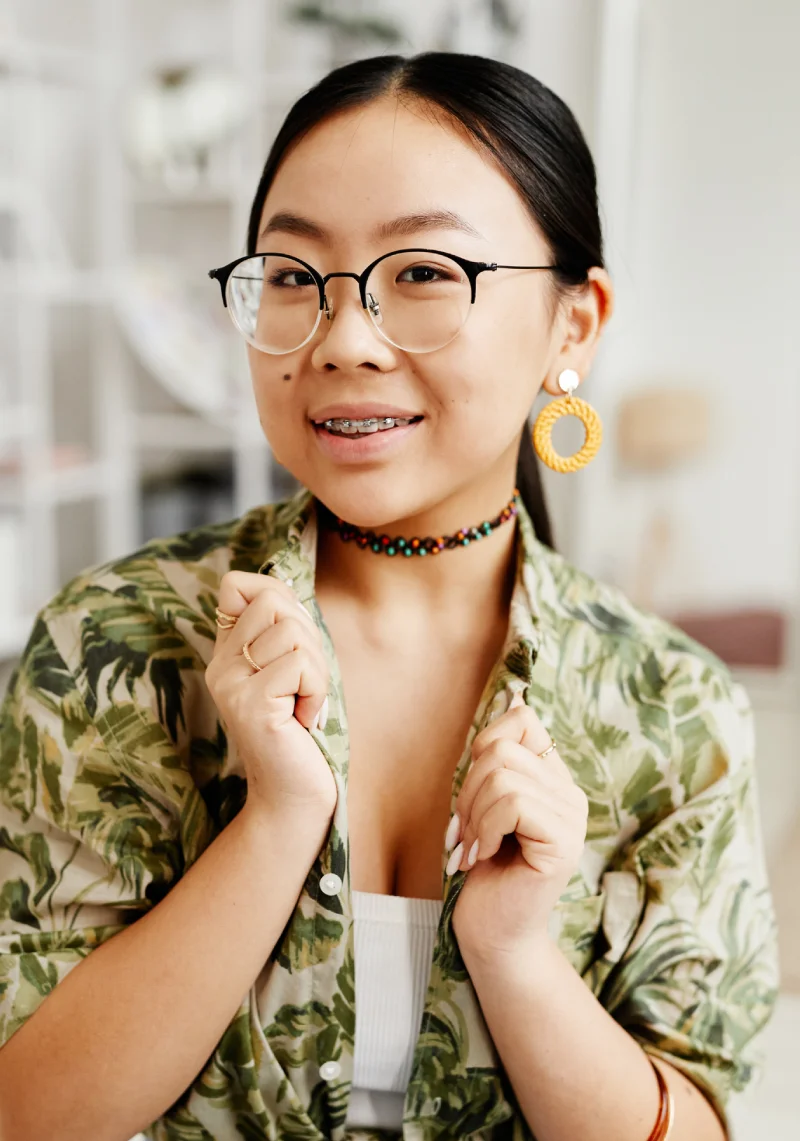 Smiling young woman in glasses with metal braces and a beaded choker