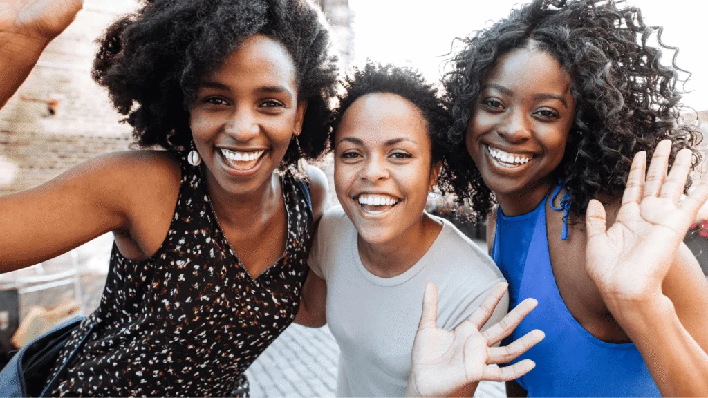 Three smiling young women waving at the camera outdoors